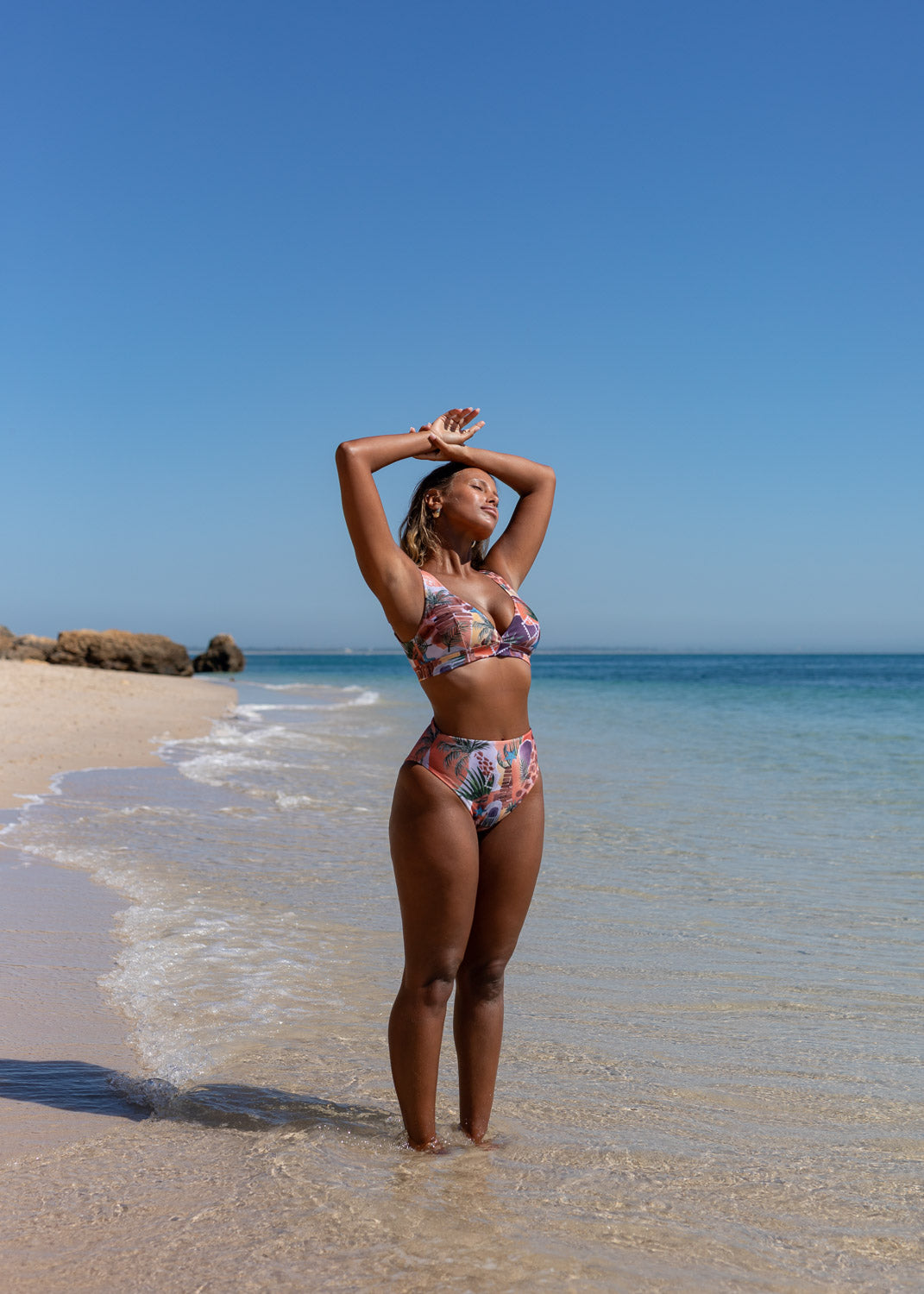 Printed high-leg bottoms by Lilja the Label with a tropical motif, worn on a sandy beach.