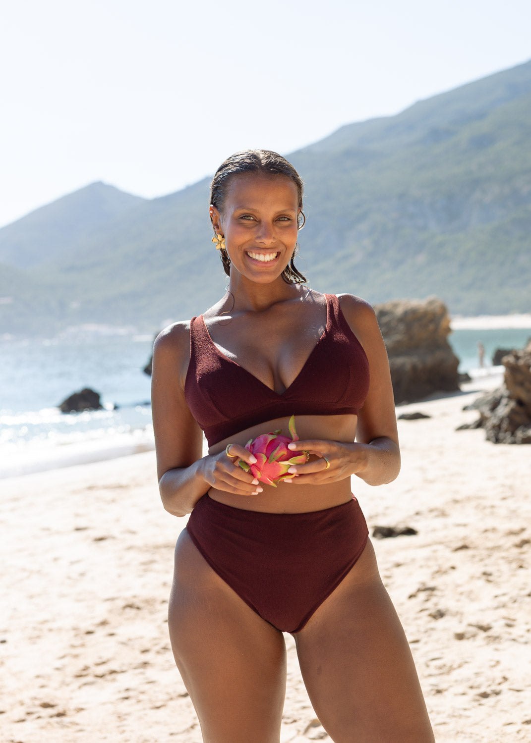 Brown plunge top by Lilja the Label with a subtle texture, styled with matching bottoms, and earrings, on a beach.