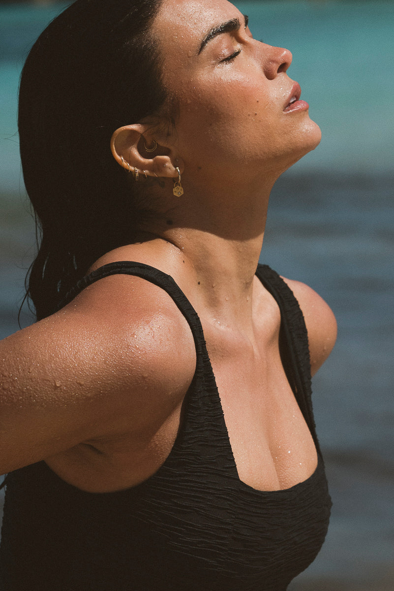 Black onepiece by Lilja the Label with a textured weave, worn outdoors with gold hoop earrings.