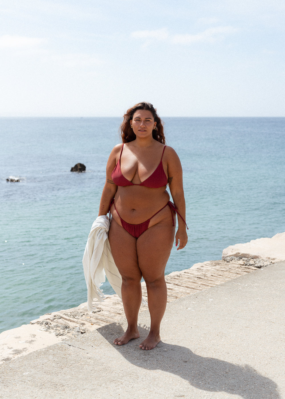 Bordeaux tie bottoms by Lilja the Label with string ties at the hips, worn on a concrete dock.