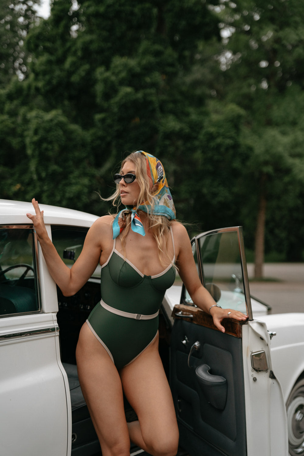 Green Linda onepiece by Lilja the Label worn with a patterned headscarf, next to a vintage car.