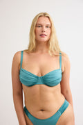 Teal gathered bikini top with thin straps and ruched cups, worn by a blonde model against a white background.