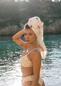 Printed bath towel from Lilja the Label with an all-over floral pattern, wrapped around a woman's head near water.