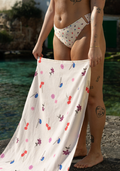 Floral bath towel by Lilja the Label featuring a colorful allover floral pattern, held by a person with tattoos.